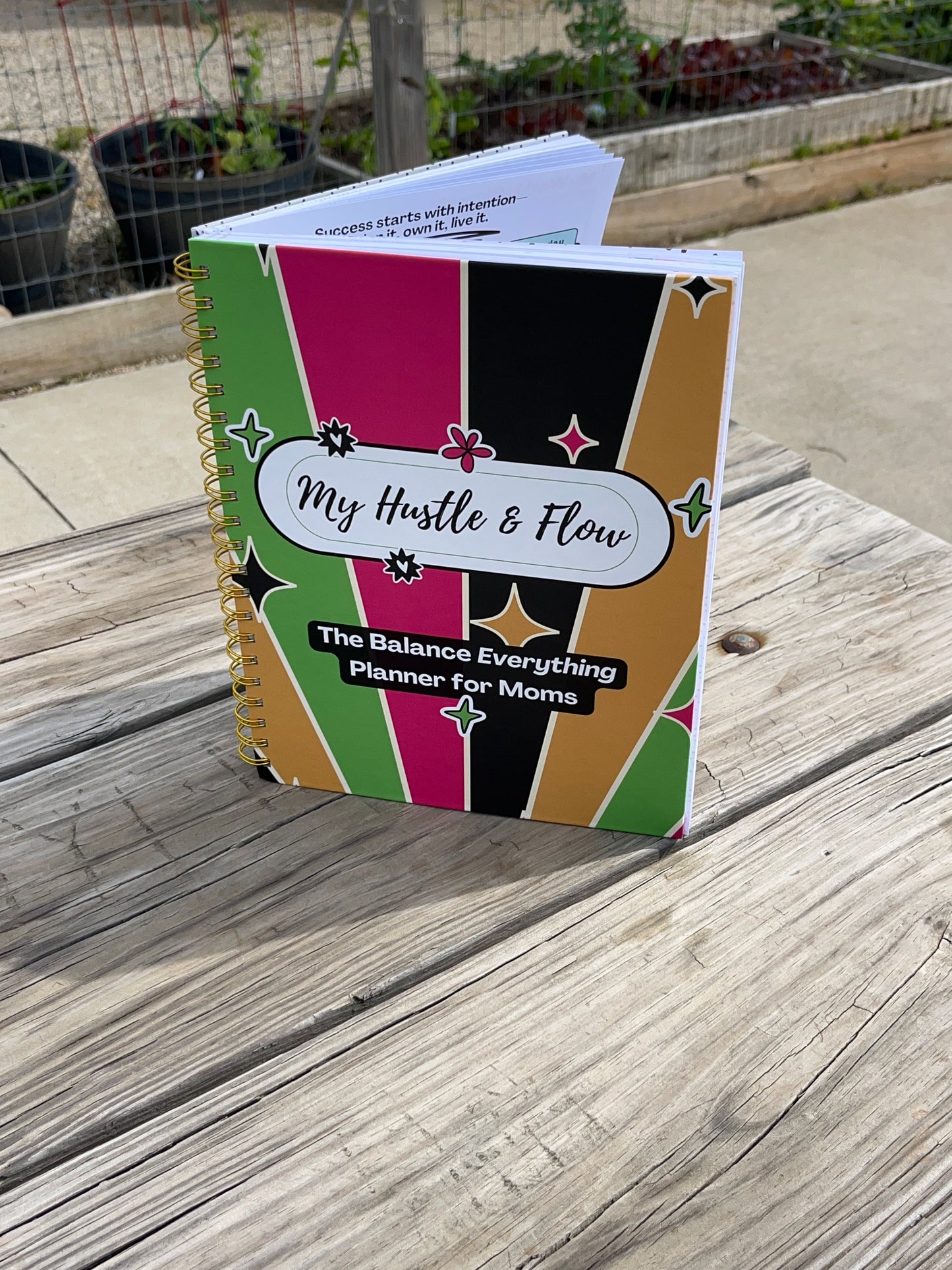 Hustle & Flow Planner displayed on a picnic table featuring bold, feminine branding designed for busy moms and creators.