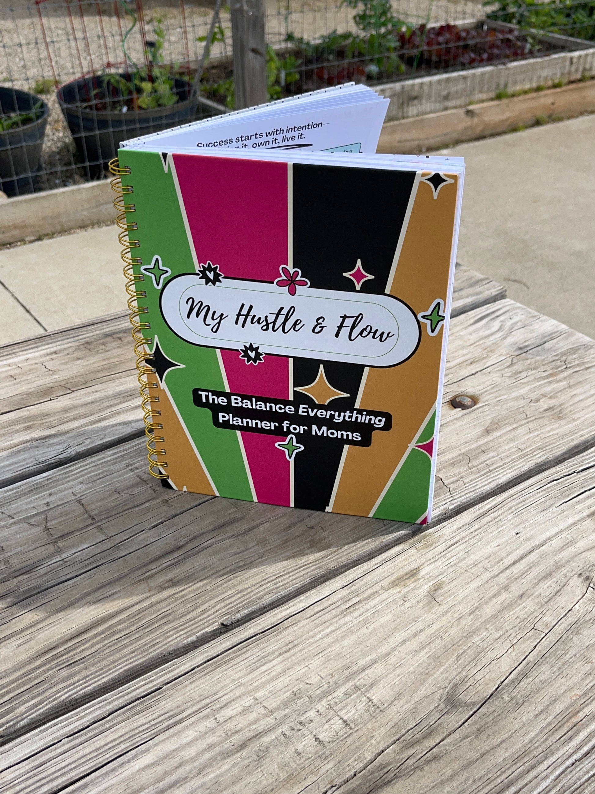 Hustle & Flow Planner displayed on a picnic table featuring bold, feminine branding designed for busy moms and creators.