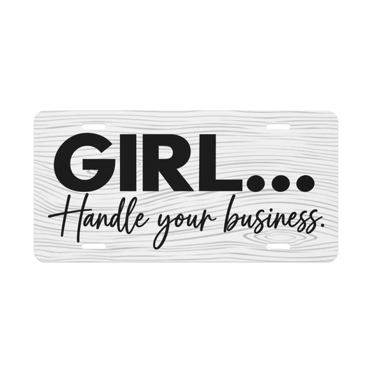 Custom white wood grain textured vanity license plate featuring black printed text with a bold 'GIRL…' on the top line and a scripted 'Handle your business.' below it. The plate includes standard pre-drilled mounting holes for installation.